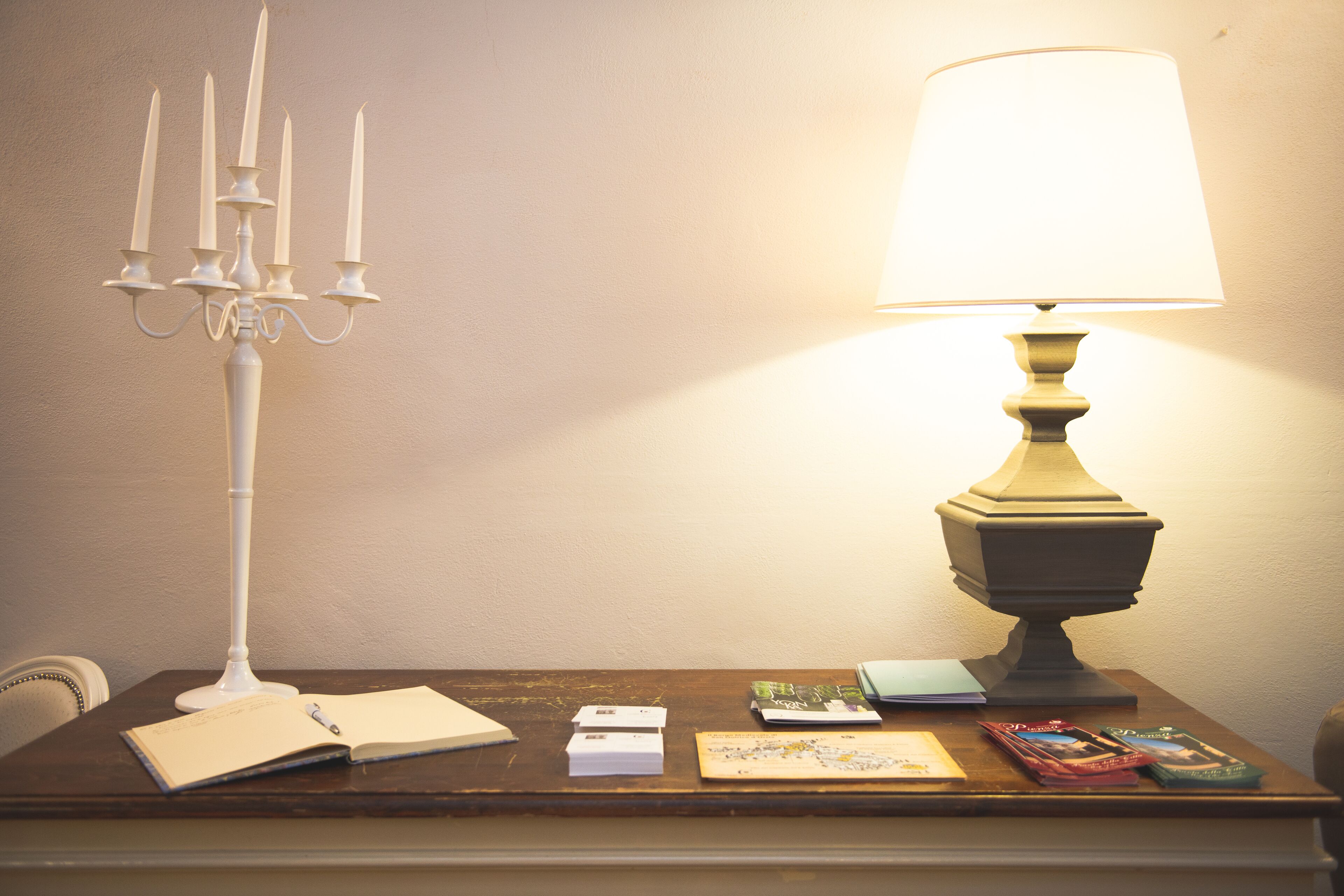 Una mesa con un candelabro blanco, una lámpara, varios libros y papeles.