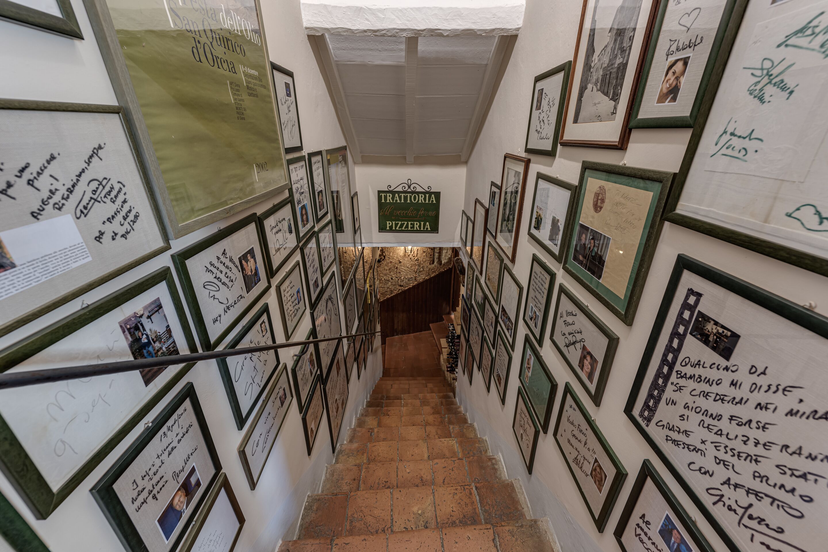 A staircase with framed photos and messages on the walls, leading to a pizzeria.