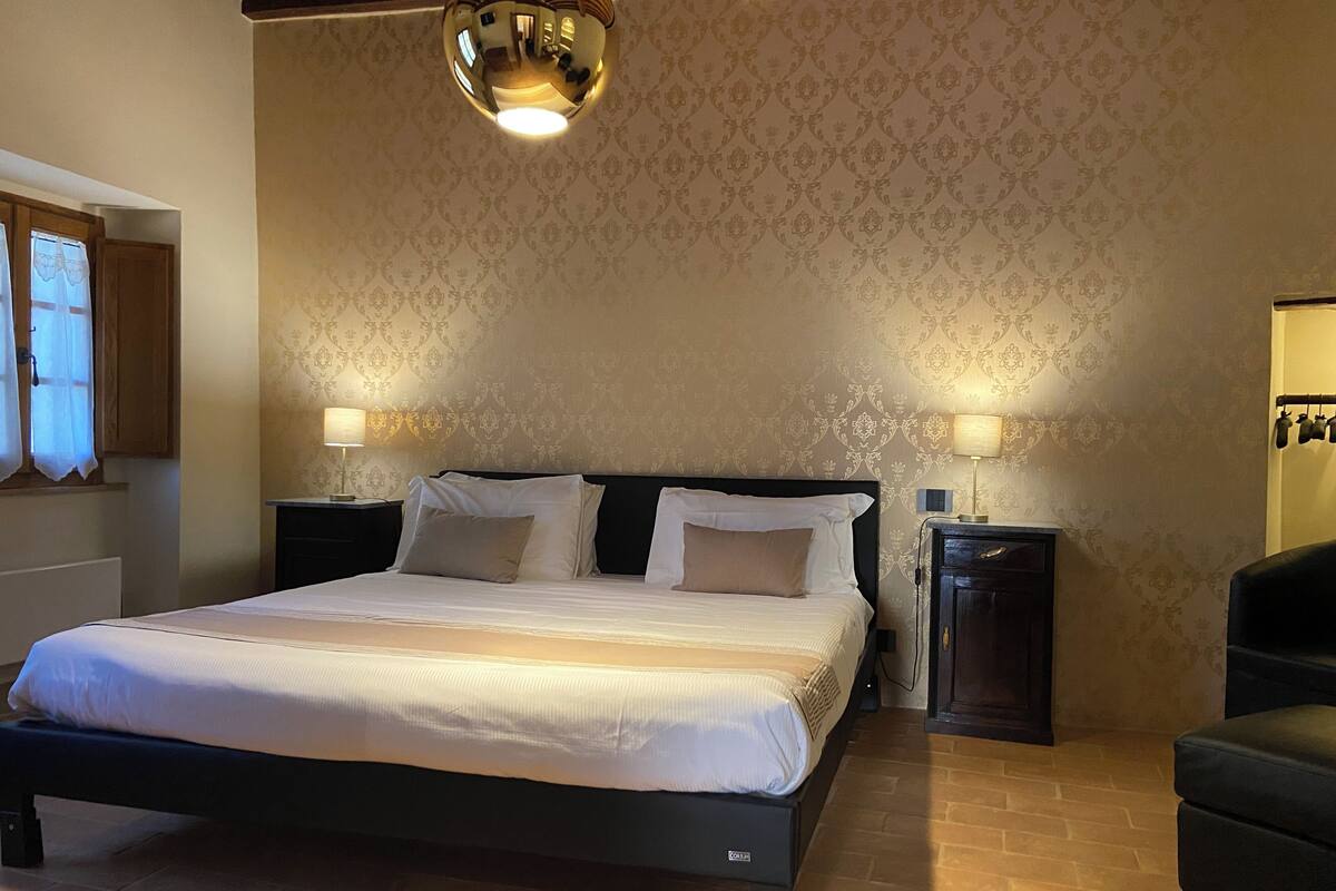 Een slaapkamer met een groot bed, twee nachtkastjes, een spiegel en een hanglamp.