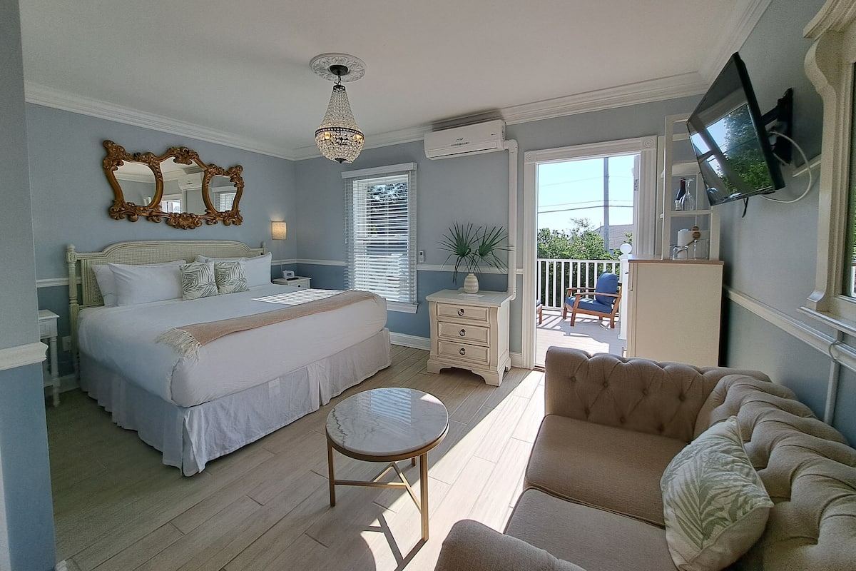 Quarto com cama, mesa de cabeceira, cômoda, televisão e varanda.