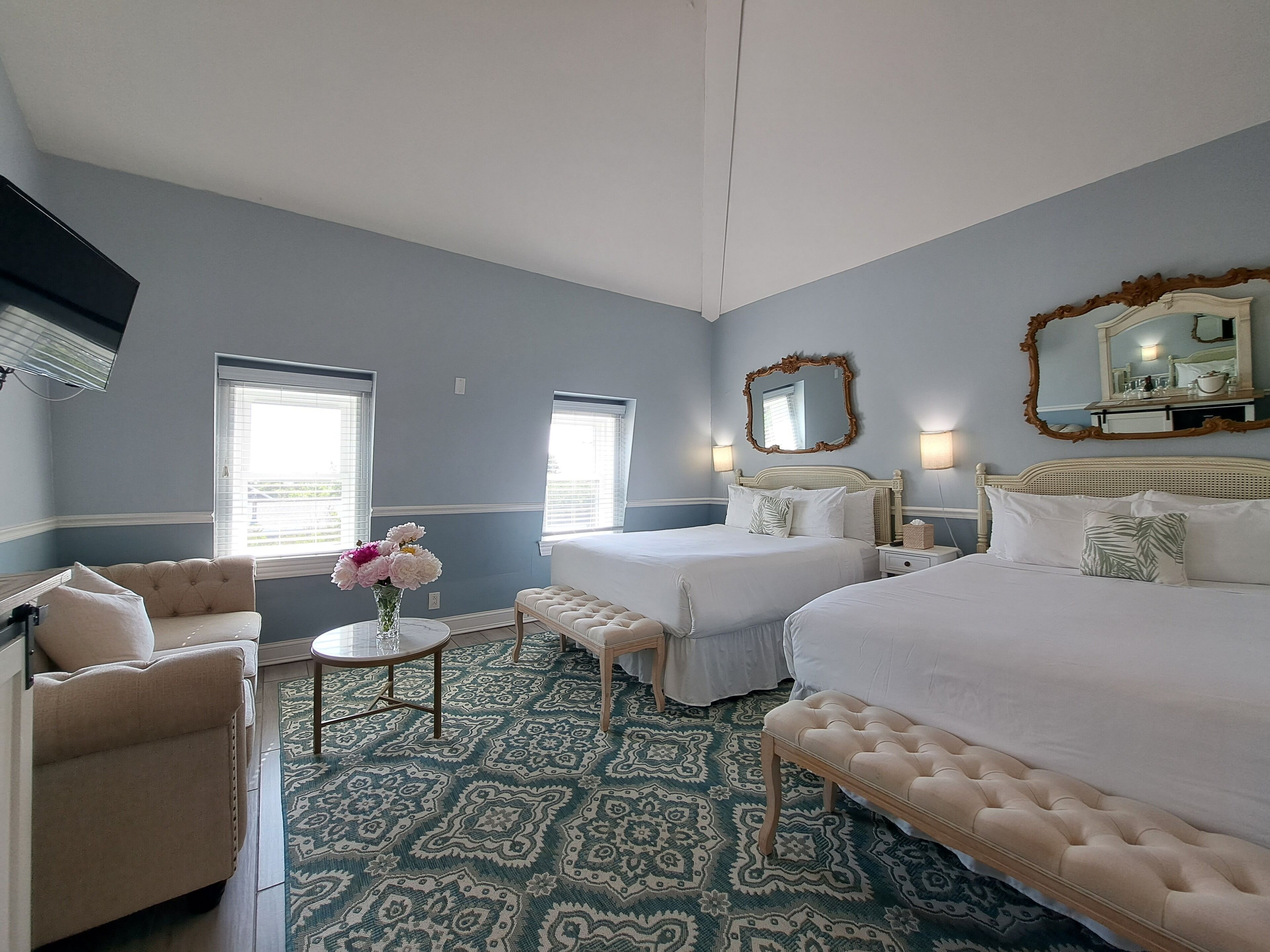 A hotel room with two beds, a sofa, a small table with flowers, and a patterned carpet.