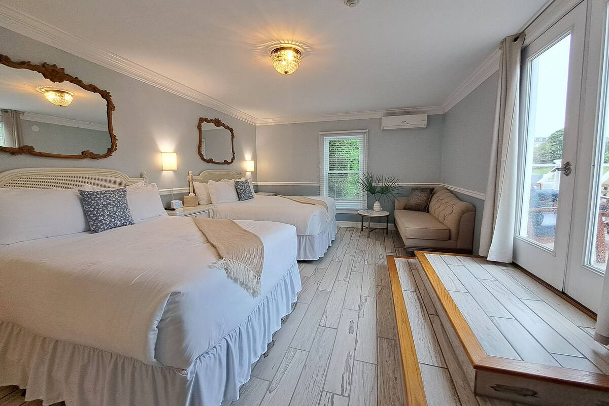Quarto de hotel com duas camas, um sofá, uma mesinha e janela com vista.