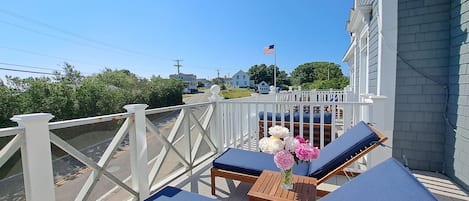 A balcony with two lounge chairs, a small table, and a vase of flowers.