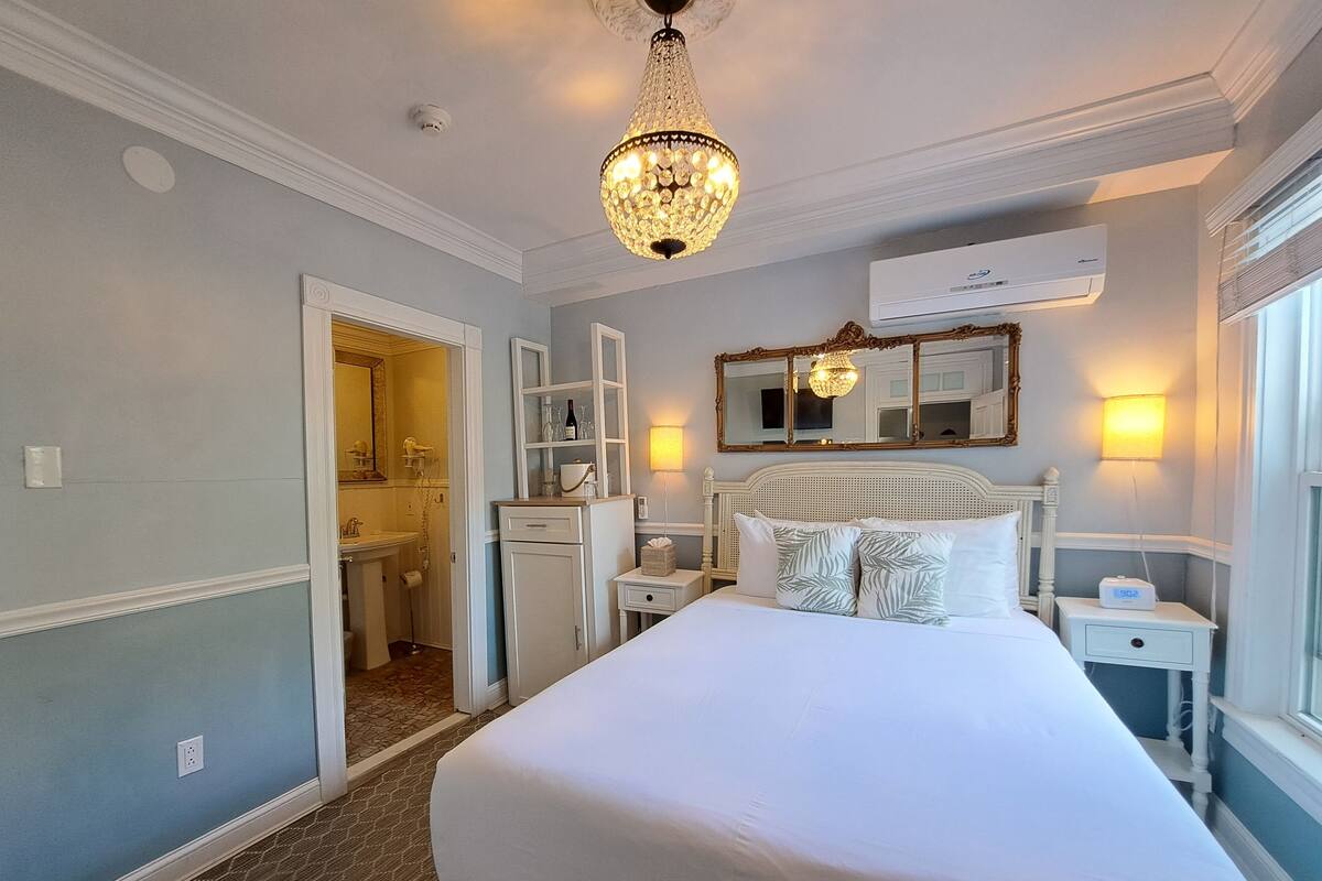 Quarto de hotel com uma cama grande, um candelabro, um espelho e um ar condicionado.