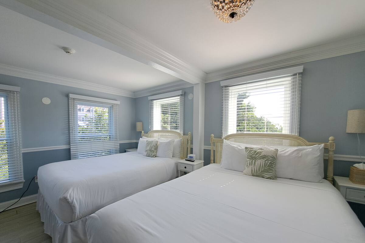 Quarto com duas camas de solteiro, roupa de cama branca e um lustre.