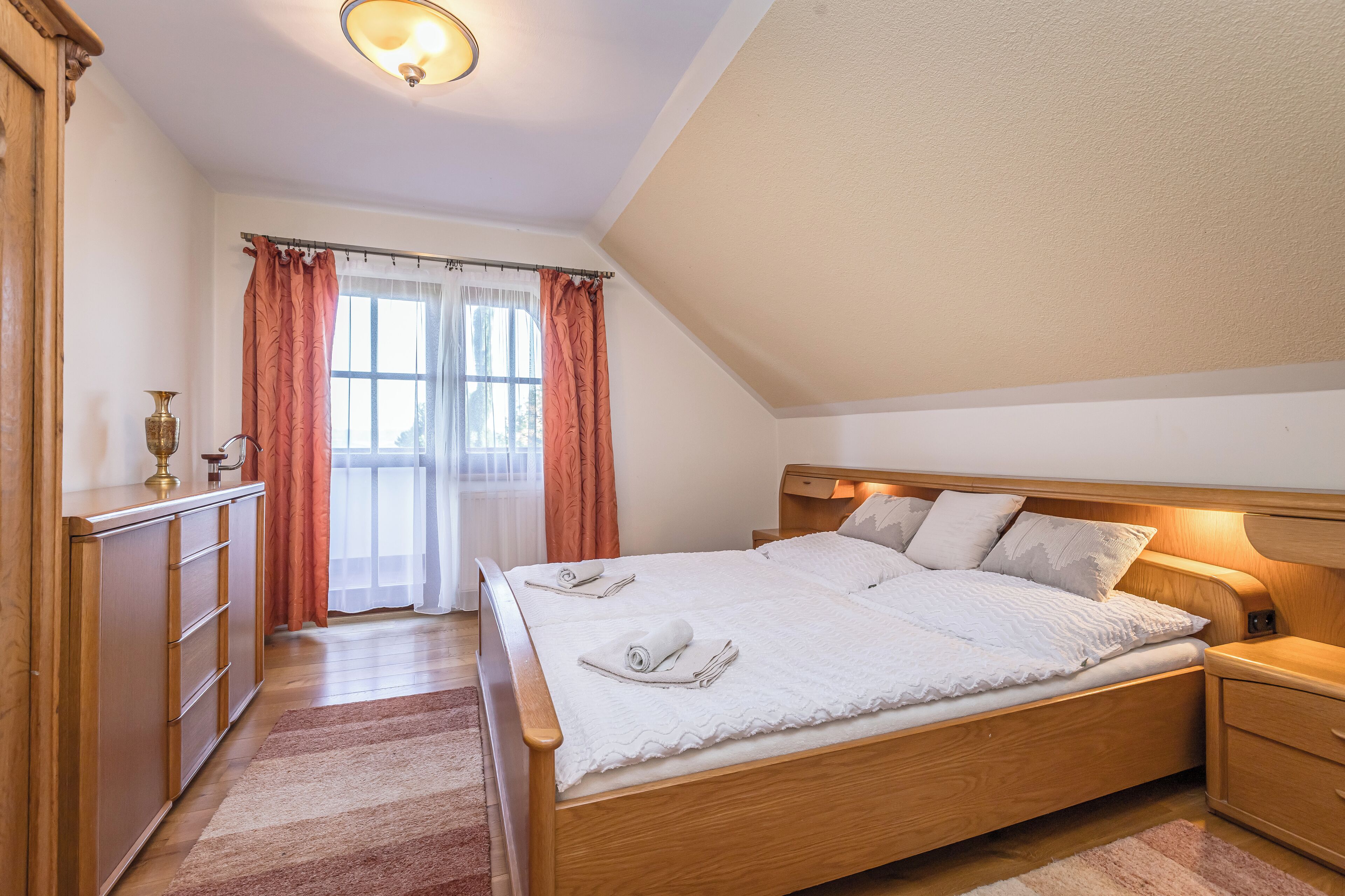Un dormitorio con cama de madera, una mesita de noche, un aparador y una ventana con cortinas.