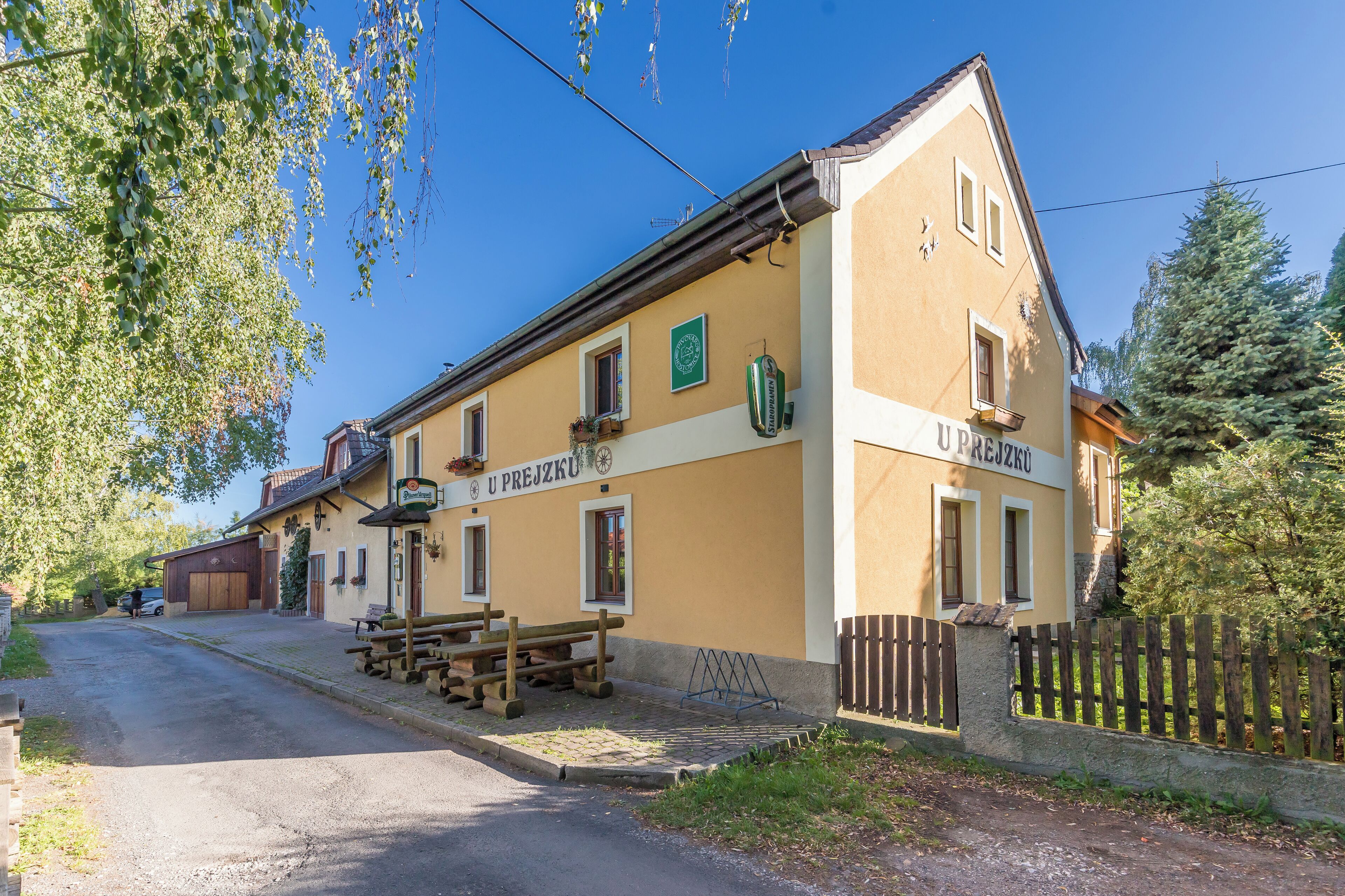 A two-story building with a yellow facade and a sign reading "UPREJZKU".