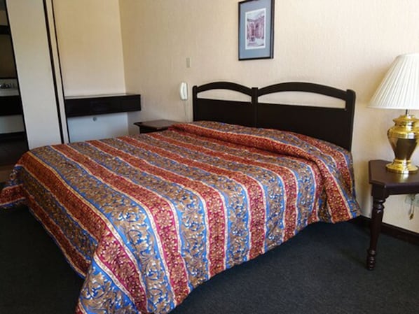 Una cama bien hecha con una colcha estampada, una mesita de noche con una lámpara y un cuadro en la pared.