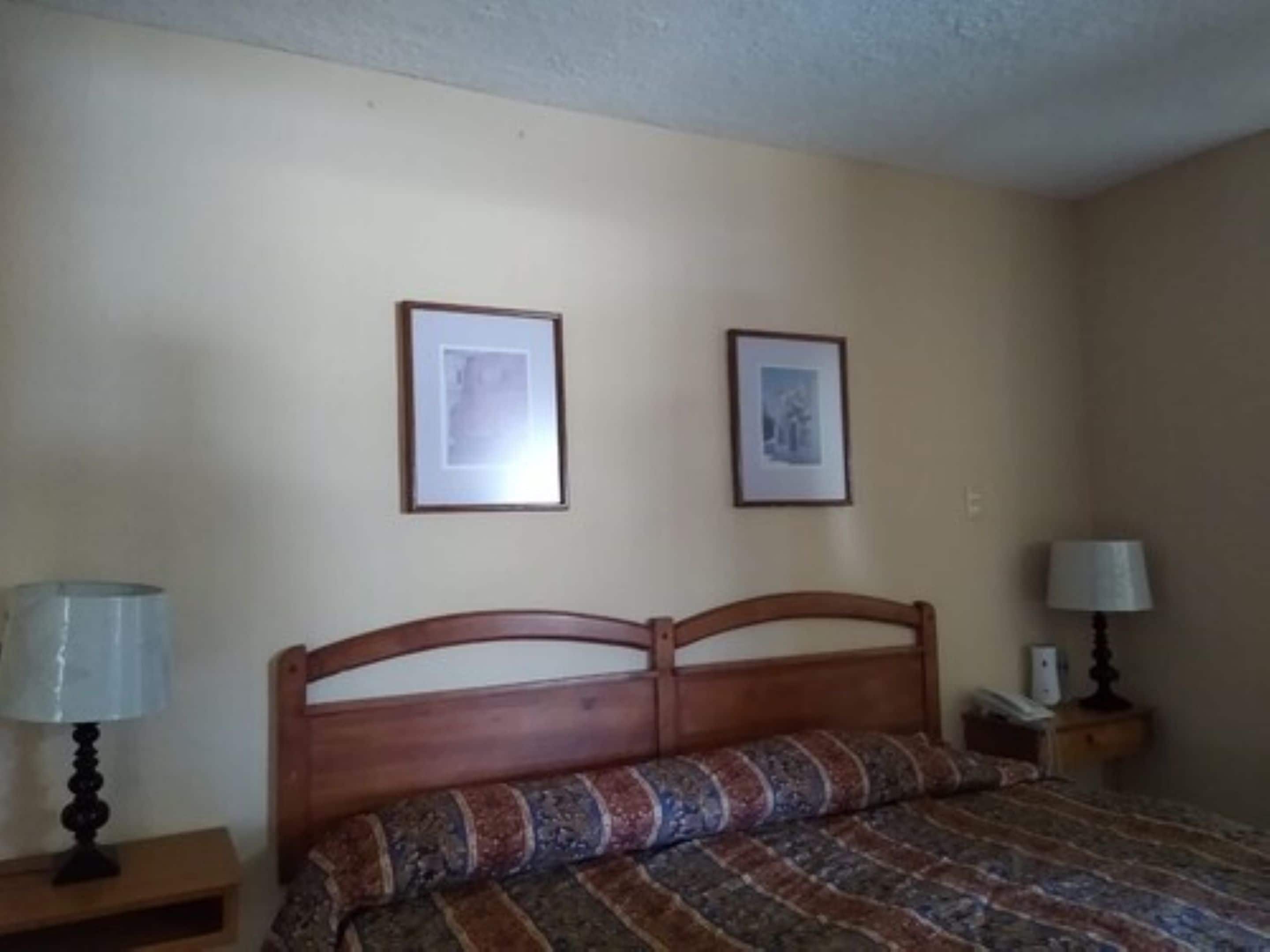 Une chambre à coucher avec un lit en bois, deux tableaux encadrés au mur, une lampe de chevet et une table de chevet.