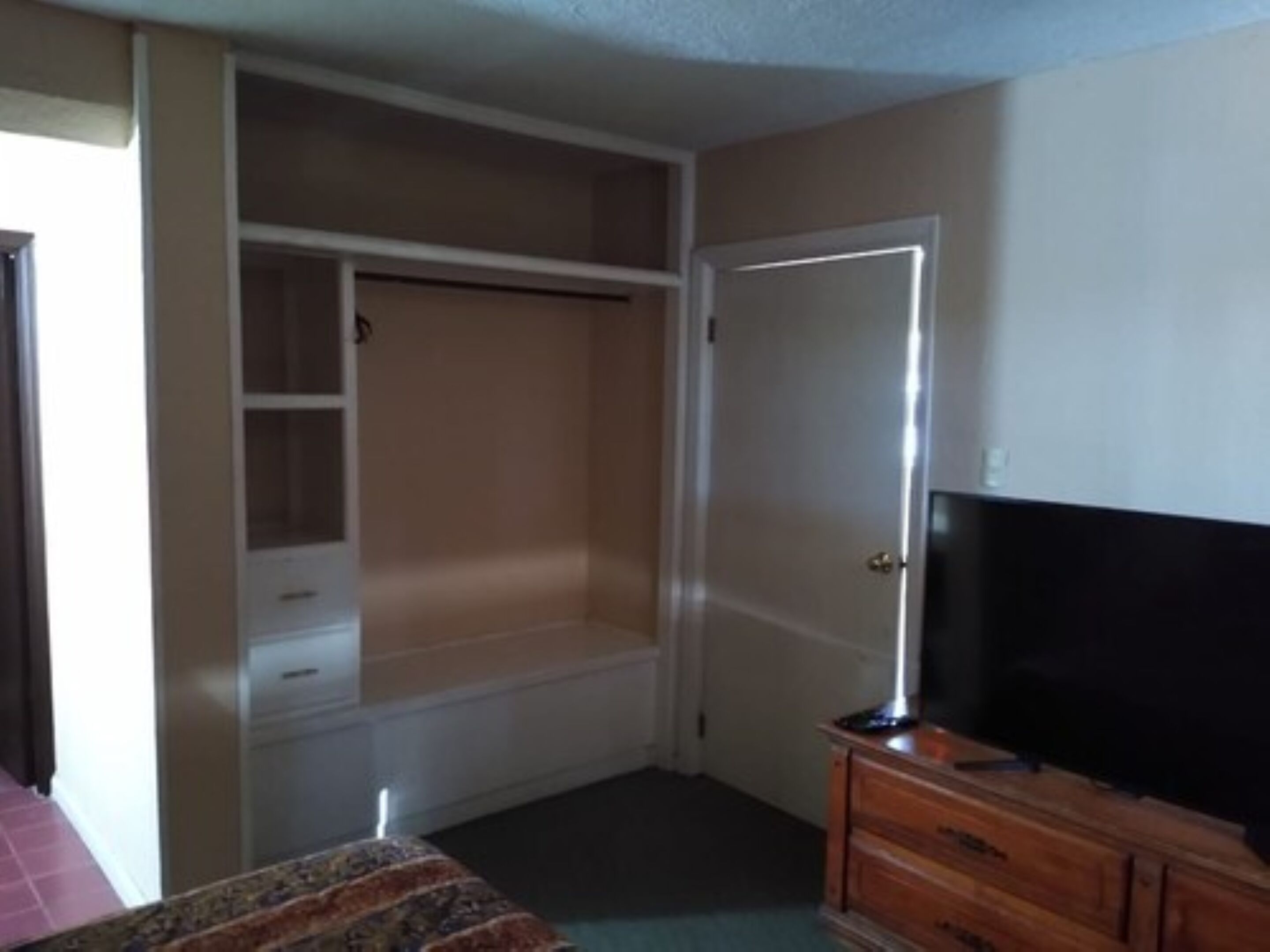 Une chambre à coucher avec un lit, une commode, une télévision et un placard.
