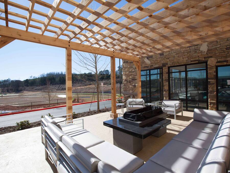 An outdoor patio with a pergola, seating area, and a stone wall with large windows.