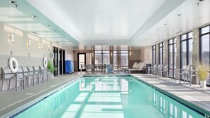 En modern inomhuspool med klart vatten, omgiven av solstolar och en sittgrupp.
