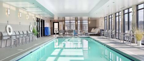 A modern indoor swimming pool with clear water, surrounded by lounge chairs and a seating area.