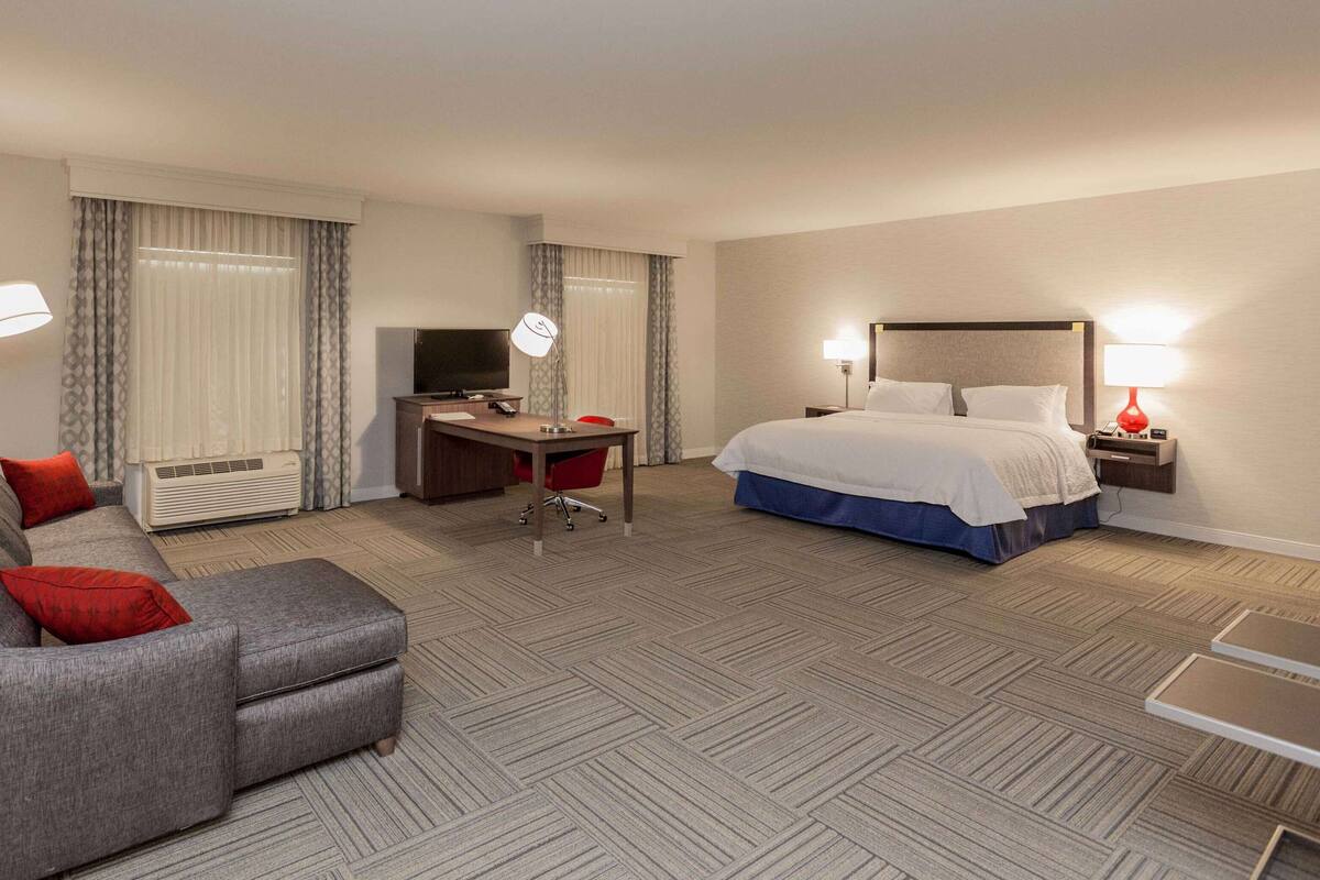 A hotel room with a sofa, a bed, a desk with a TV, and a lamp.