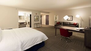 Ett hotellrum med en stor säng, ett skrivbord, en röd stol, en soffa och en lampa.