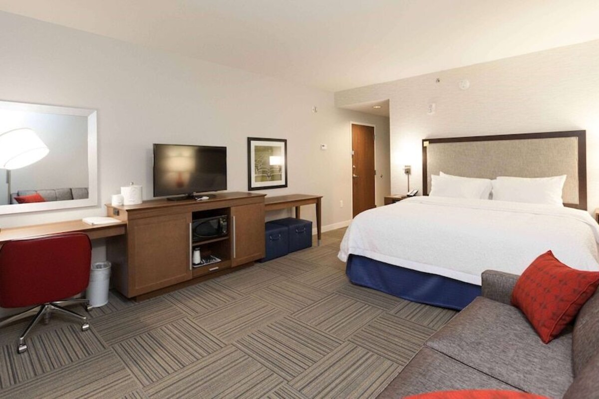 A hotel room with a large bed, a desk with a TV, a chair, and a sofa.
