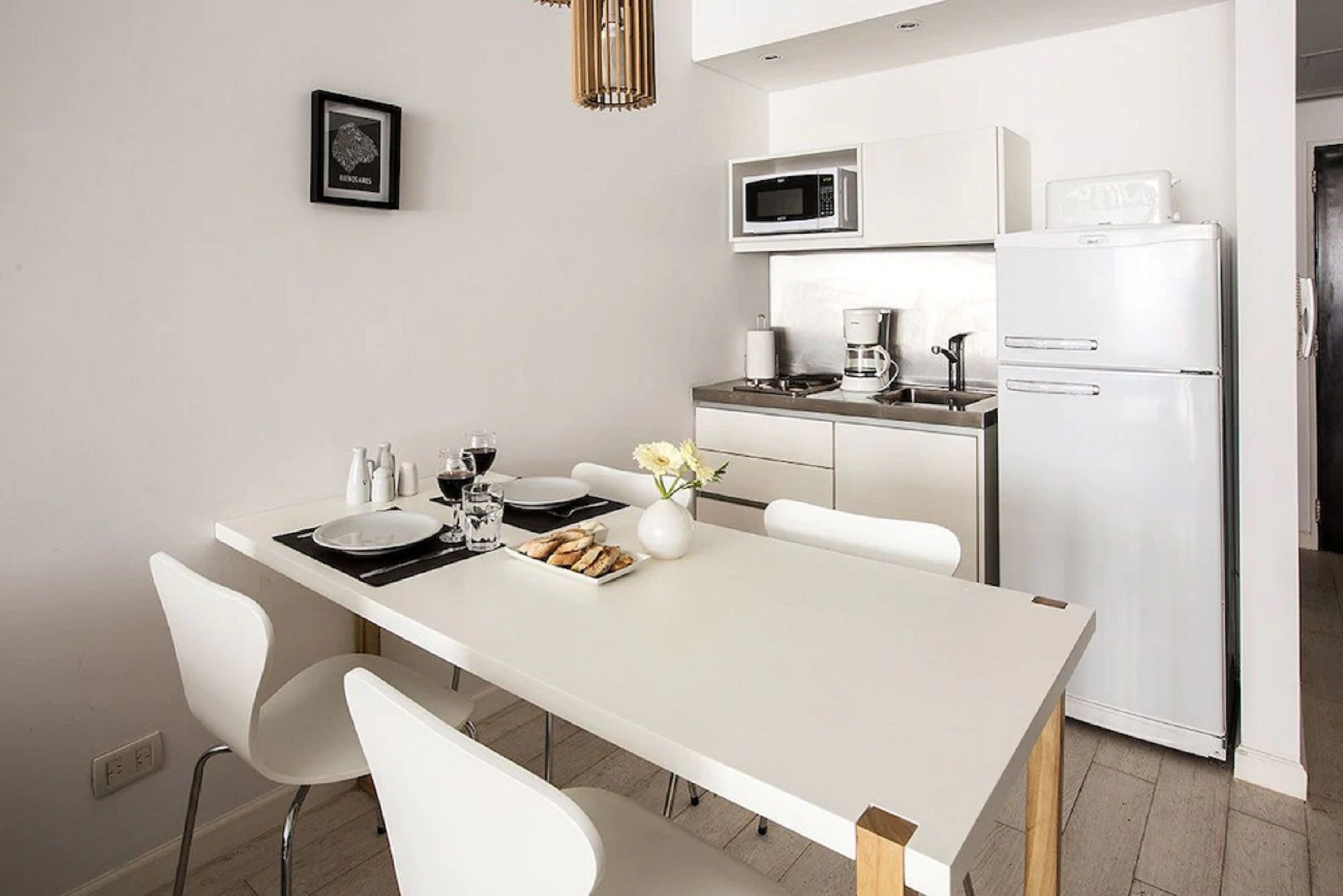 A modern kitchen with white appliances, a dining table with chairs, and a small decorative vase.