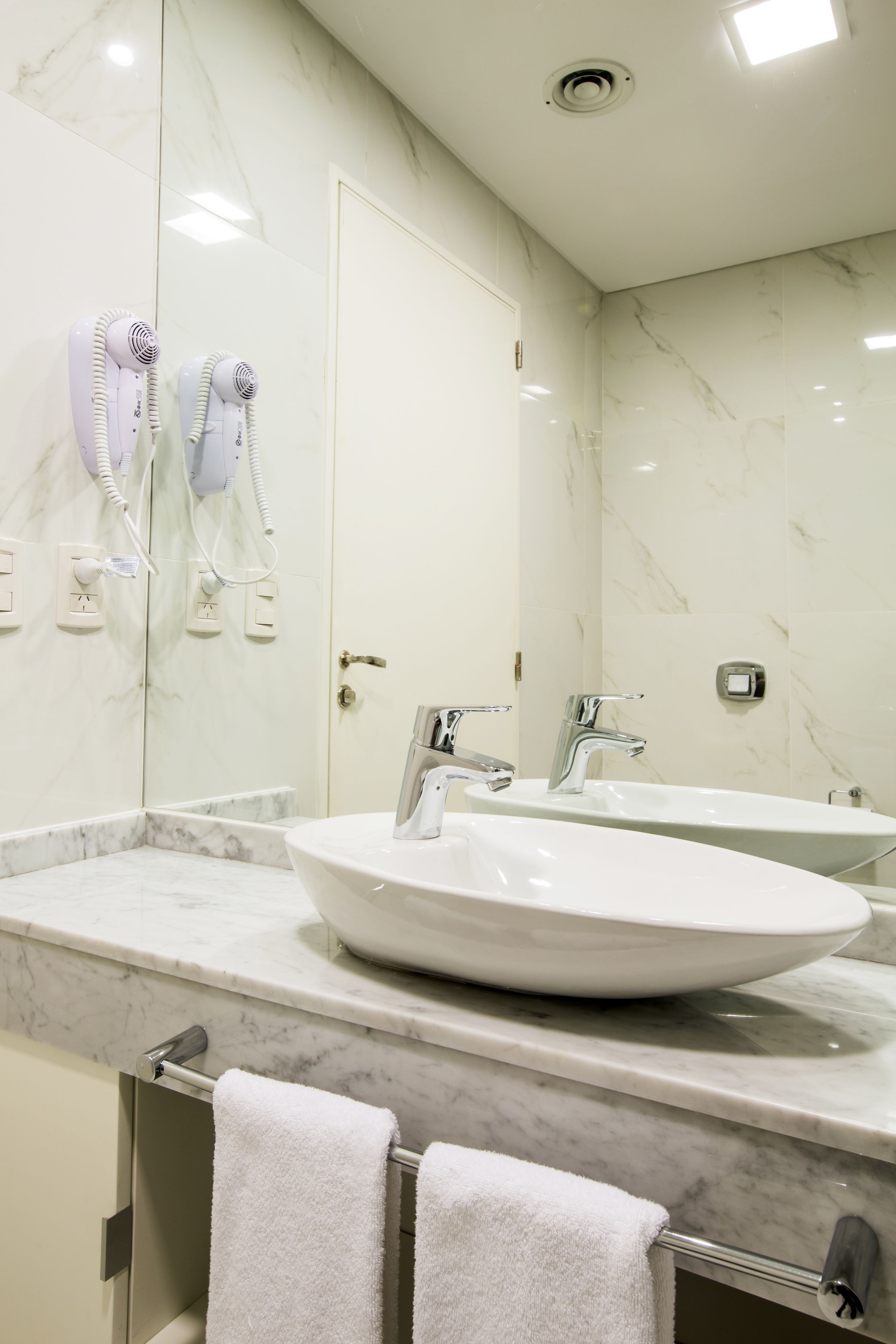 Een moderne badkamer met een witte wasbak, twee spiegels, een handdoekhouder en een marmeren wand.