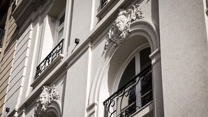 Fachada de edificio con detalles arquitectónicos ornamentales, incluyendo molduras decorativas y balcones de hierro forjado.