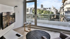 Una sala de estar moderna con un ventanal grande, un televisor de pantalla plana, una mesita con un libro y un tapete redondo.