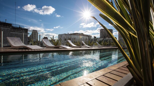 Una piscina con tumbonas para tomar el sol y un paisaje urbano de fondo.