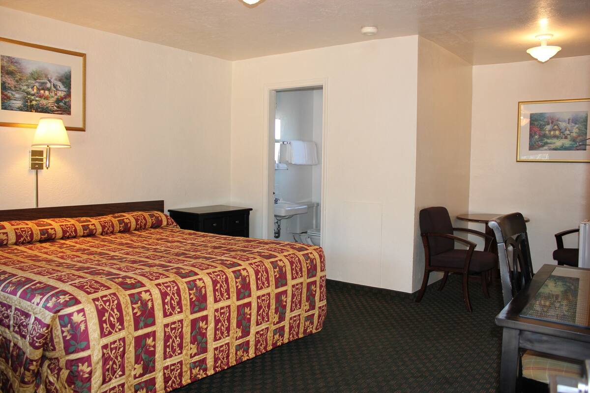 A hotel room with a large bed, a desk, two chairs, a sink, and a door leading to a bathroom.