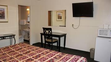 Habitación de hotel con cama, escritorio, silla, televisión, microondas, cubo de basura y baño con inodoro y lavamanos.