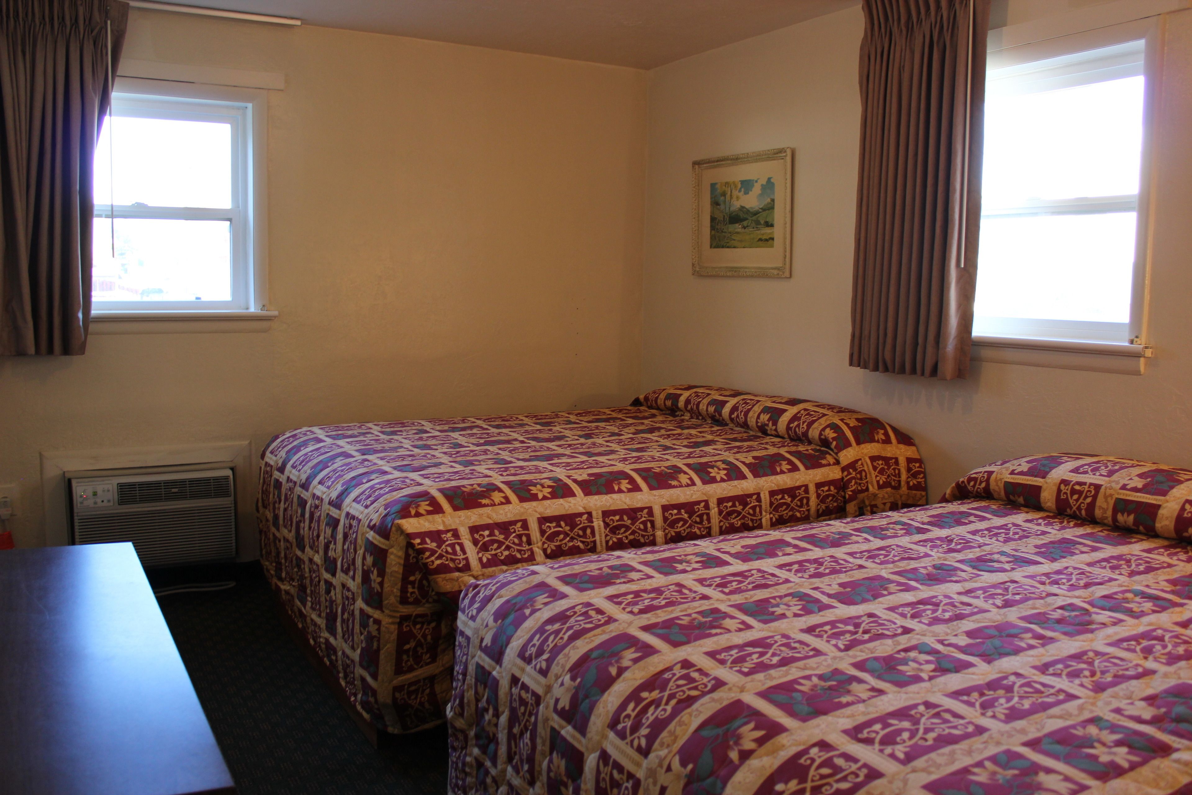 A room with two beds, a desk, and a window with curtains.