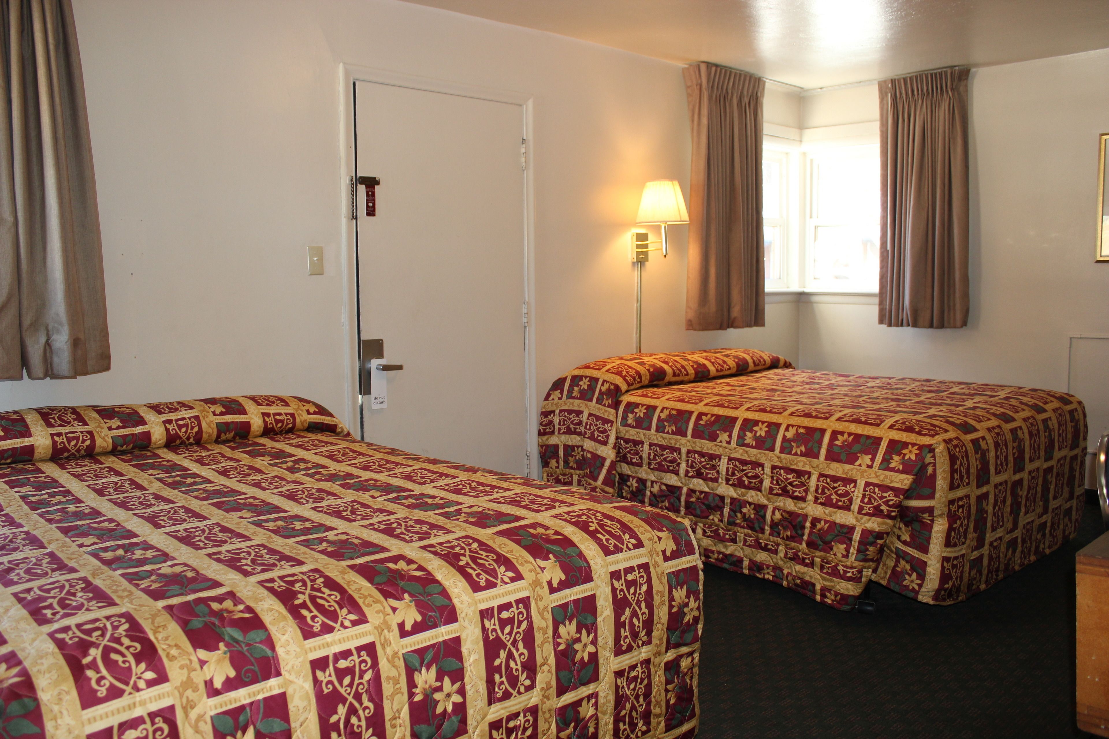 A hotel room with two beds, a door, a lamp, and a window with curtains.