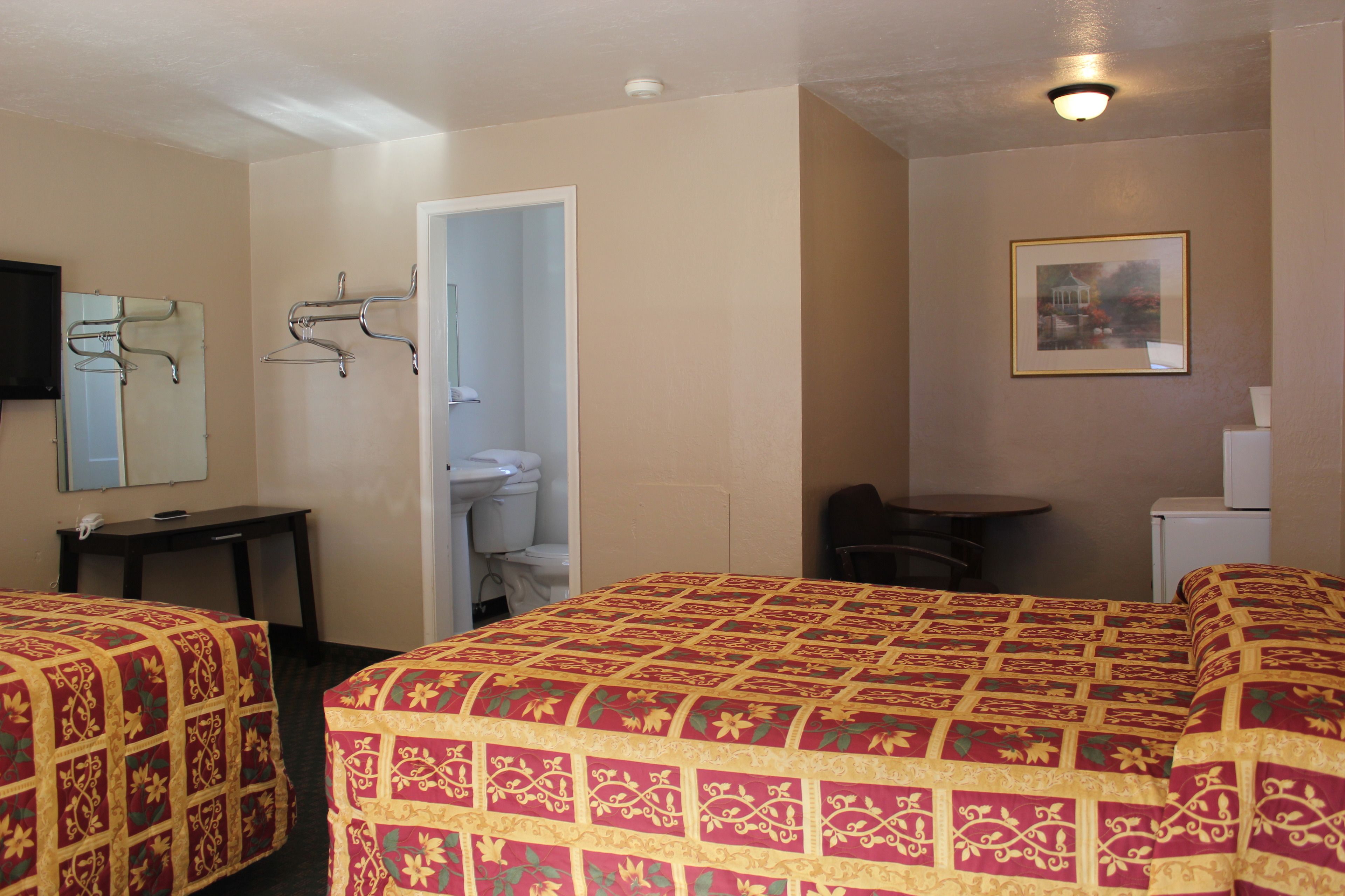 A hotel room with two beds, a desk, a chair, a TV, a coat rack, and a bathroom visible through an open door.