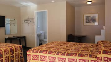 A hotel room with two beds, a desk, a chair, a TV, a coat rack, and a bathroom visible through an open door.