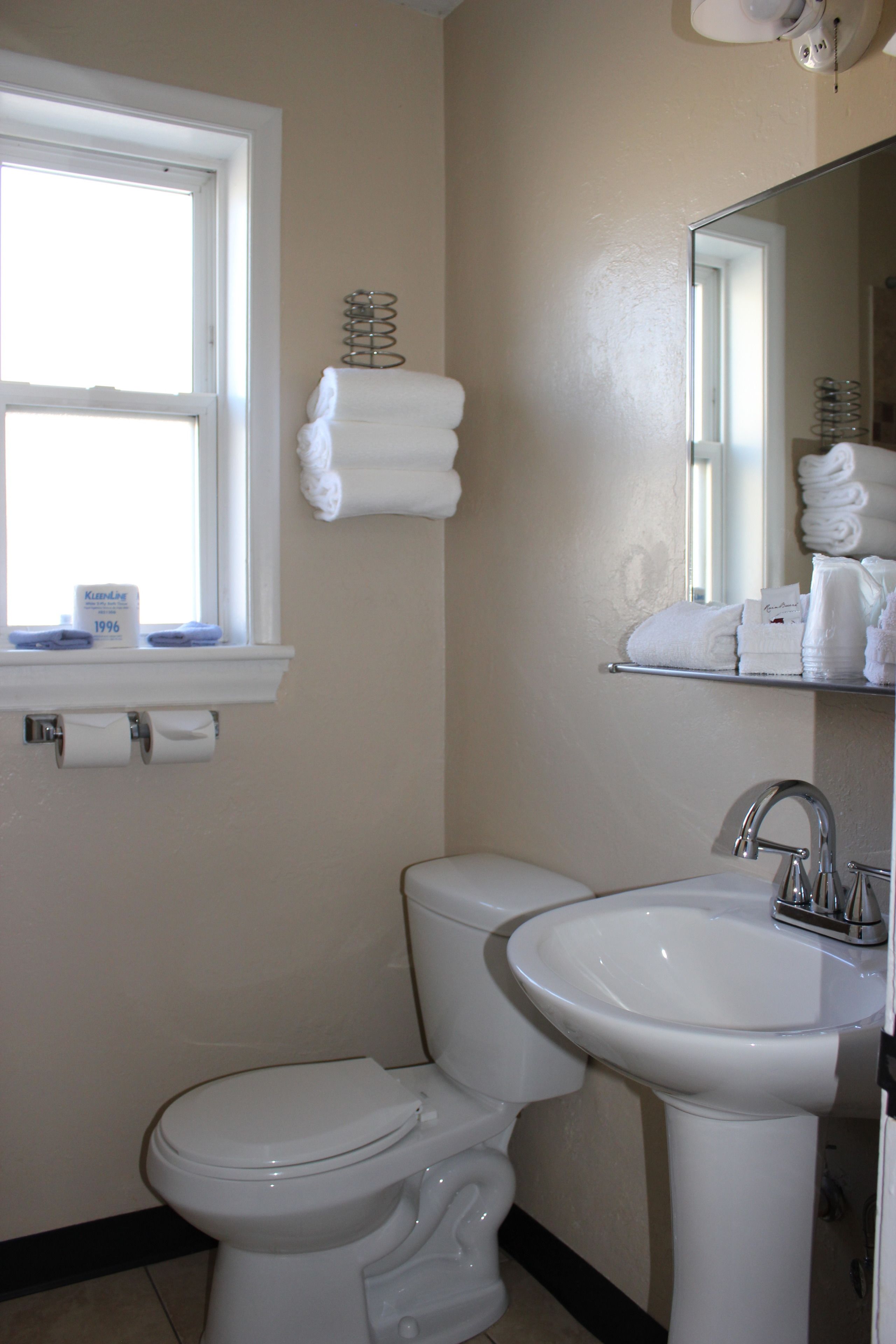 Un baño con inodoro, lavamanos y ventana con perchero para toallas.