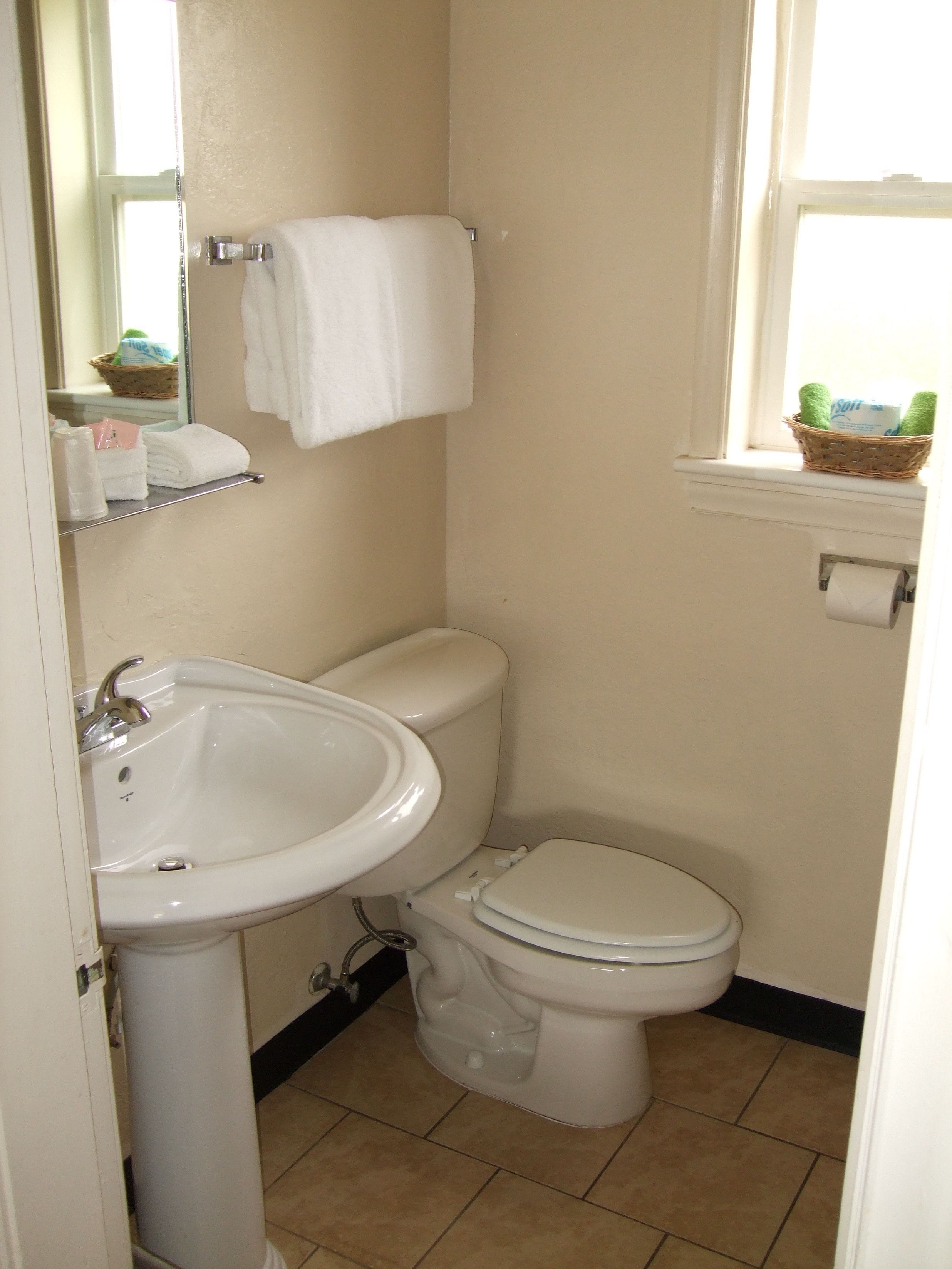 A bathroom with a white sink, toilet, and a window with a basket of green towels.