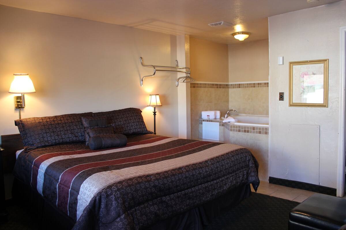 A hotel room with a large bed, bedside lamps, a bathroom with a sink and mirror, and a framed picture on the wall.