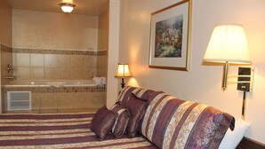 A hotel room with a large bed, a bathroom with a bathtub, and a painting on the wall. - Lava Spa Motel & RV Park (Lava Hot Springs)