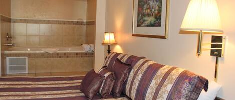 A hotel room with a large bed, a bathroom with a bathtub, and a painting on the wall.