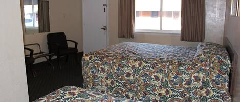 Una habitación de hotel con cama, una silla, ventana con cortinas y puerta.