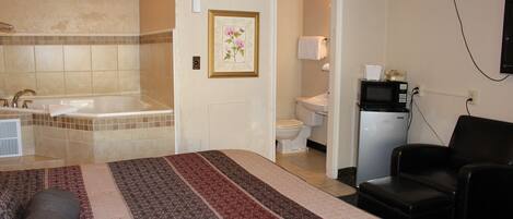 A hotel room with a large bed, a bathtub, a toilet, a microwave, and a chair.