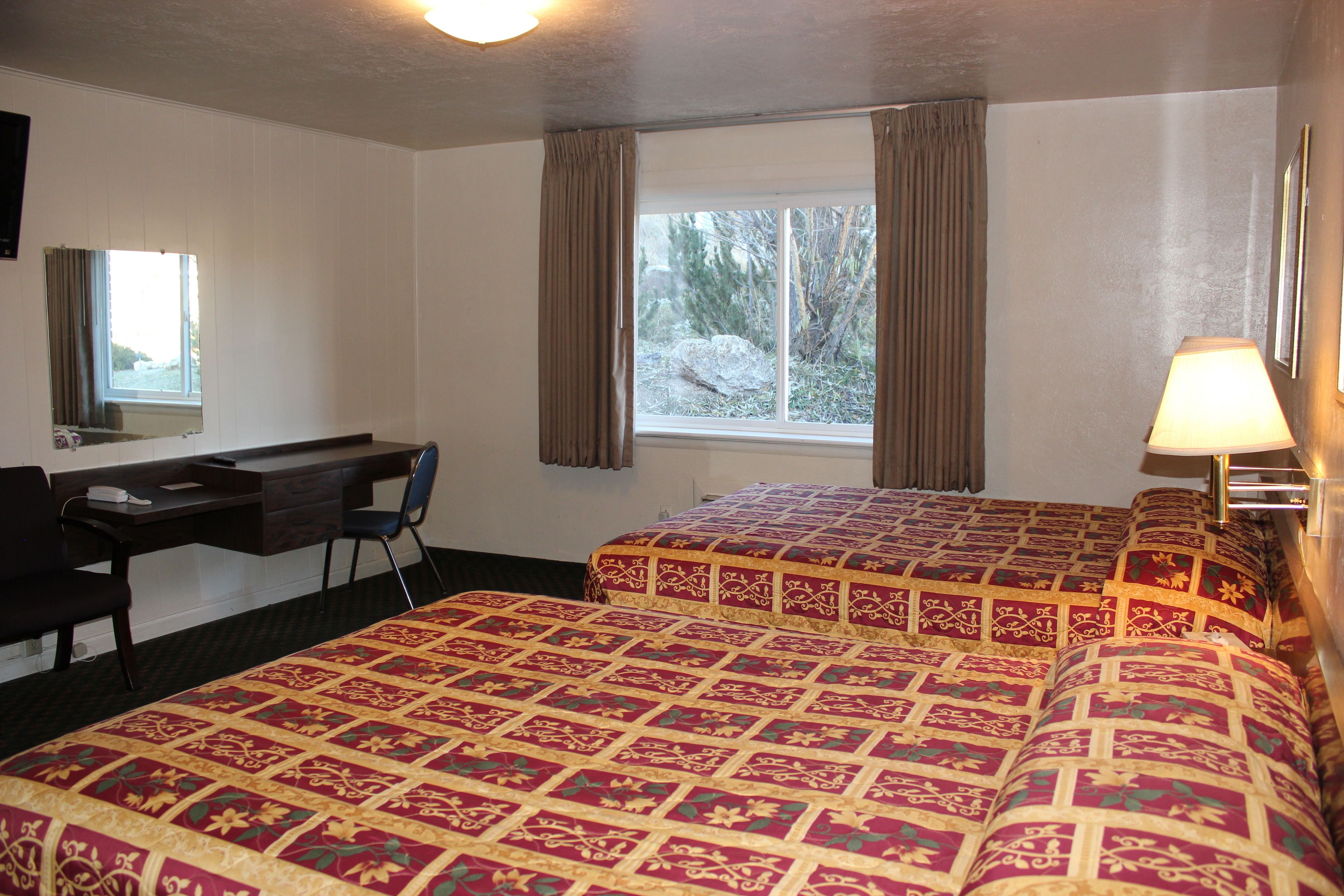 A hotel room with two beds, a desk, a chair, and a window with curtains.