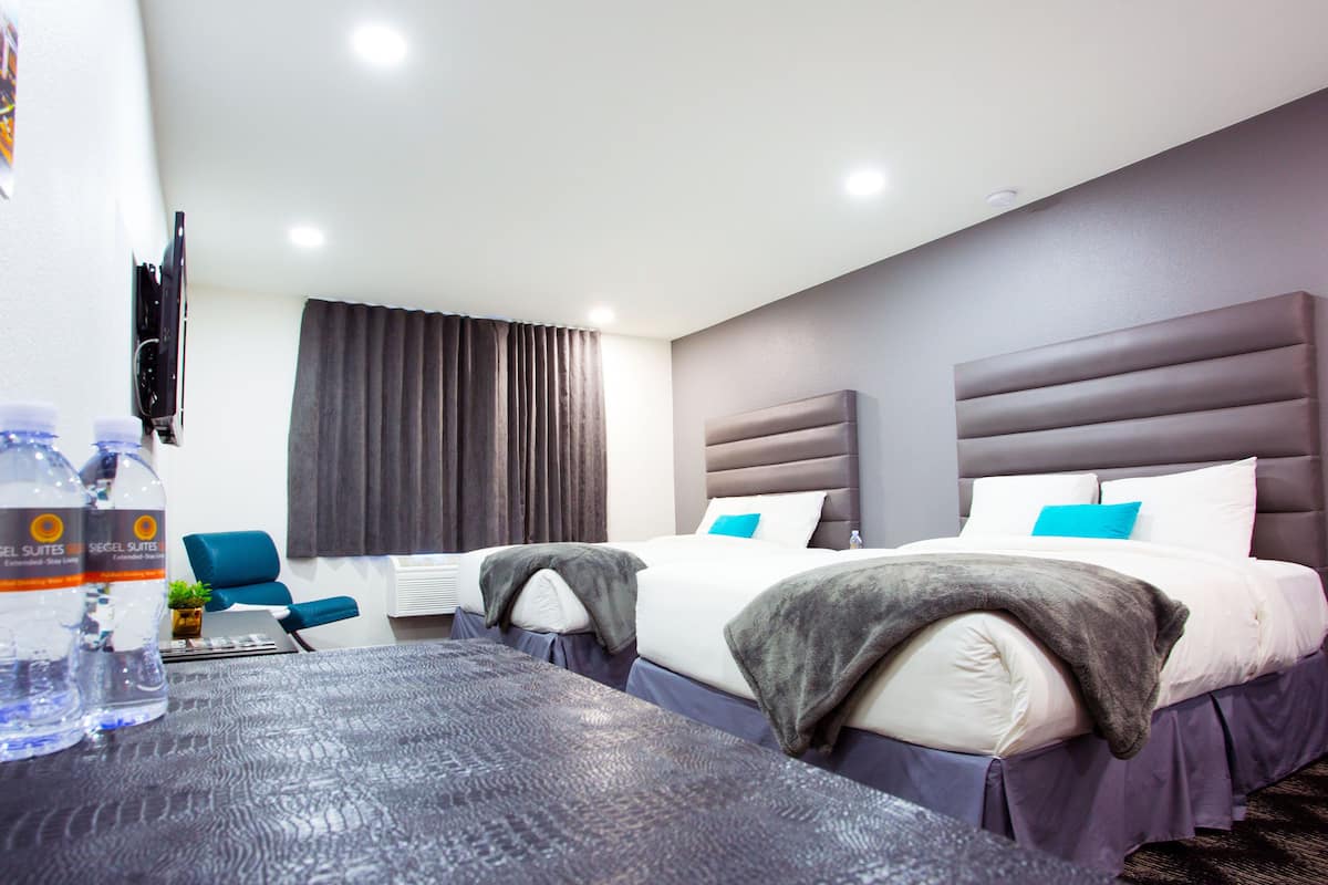 A hotel room with two beds, a desk with a chair, a TV, and a window with curtains.