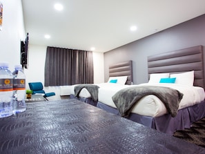 Una habitación de hotel con dos camas, un escritorio con silla, un televisor y una ventana con cortinas.