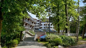 Ein Wohngebäude mit einer Treppe, die zu einem Balkon führt, umgeben von Grünpflanzen und parkenden Autos.