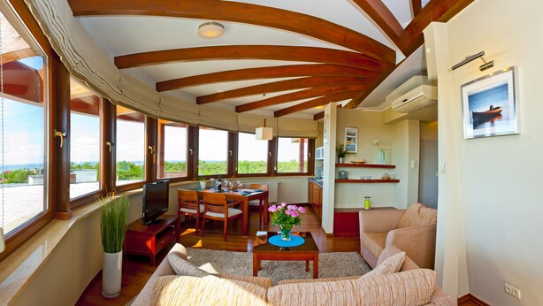 Ein geräumiger Wohnbereich mit Holzboden, großen Fenstern, einem Esstisch und einem Sofa.