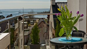 Ein Balkon mit Glastrennwand, ein Tisch mit Blumen in einer Vase und Blick auf Gebäude und Wasser.