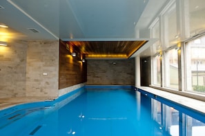 Piscina interior com teto de madeira, paredes de pedra e grandes janelas.