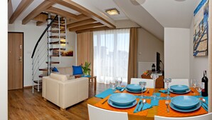Ein modernes Wohnzimmer mit Treppe, einem Essbereich mit blauen Tellern und Gläsern sowie einer Küche im Hintergrund.