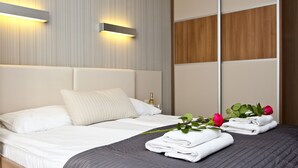 Ein ordentlich bezogenes Bett mit weißen Leinen, einer dunkelgrauen Decke und einem Holzkopfschild. Zwei Wandleuchten und ein Spiegel spiegeln den Raum wider.