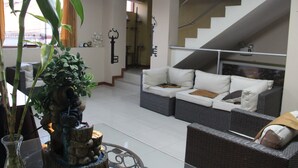 Uma sala de estar moderna com um conjunto de sofás, uma planta decorativa e uma escadaria.