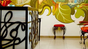 Interior de hotel com um mural de girassóis e montanhas, um candelabro e duas cadeiras vermelhas.
