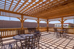 Une terrasse extérieure dotée d’une pergola en bois, de tables et de chaises.